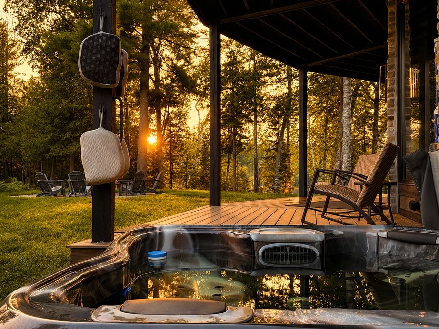 The hot tub on the deck, sun setting through the trees beyond