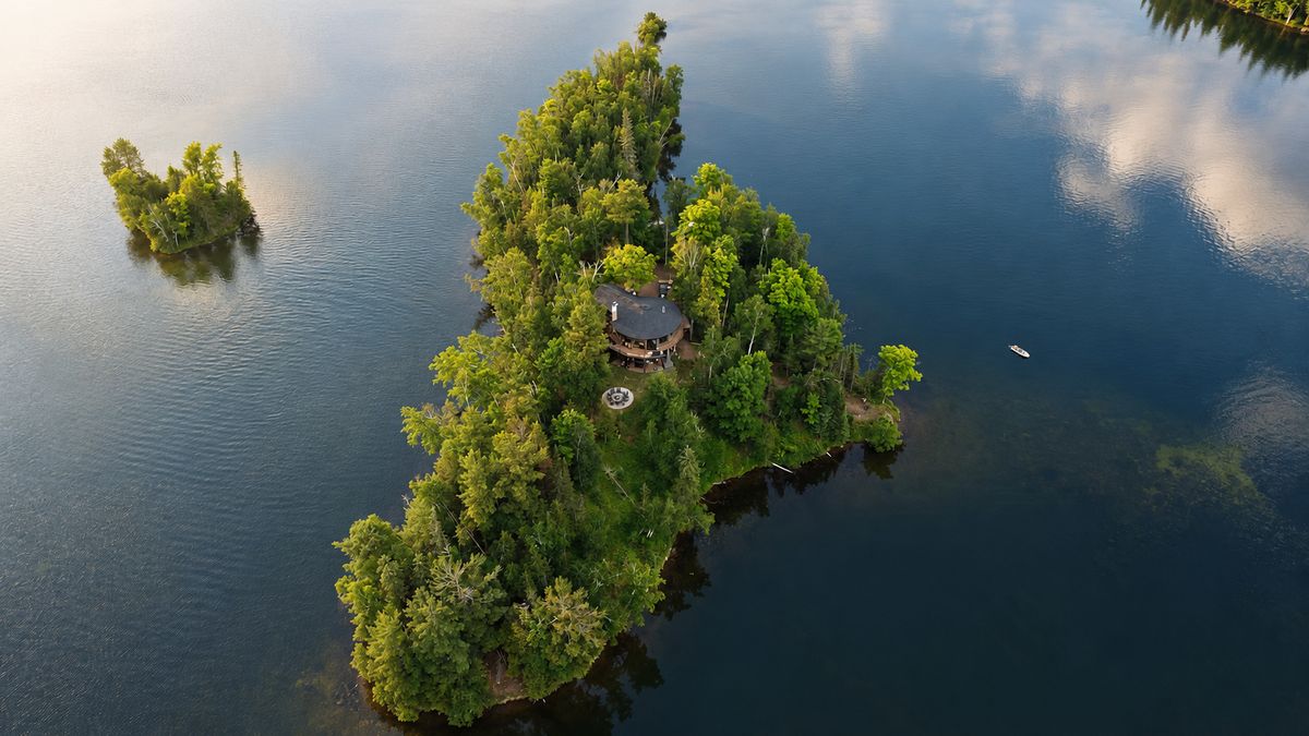 The island from above — the round house among the trees, open water on every side